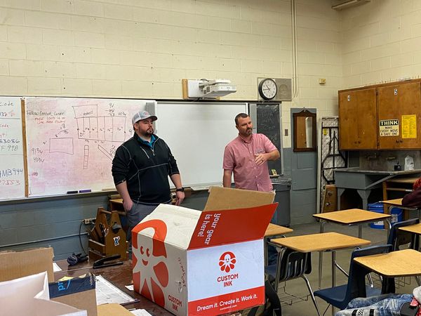 Business owner and employee at the front of a high school workshop classroom